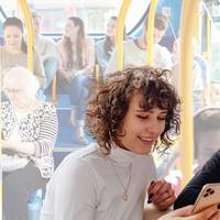 Zwei Frauen schauen auf ein Handy, im Hintergrund sitzen Fahrgäste im Bus.